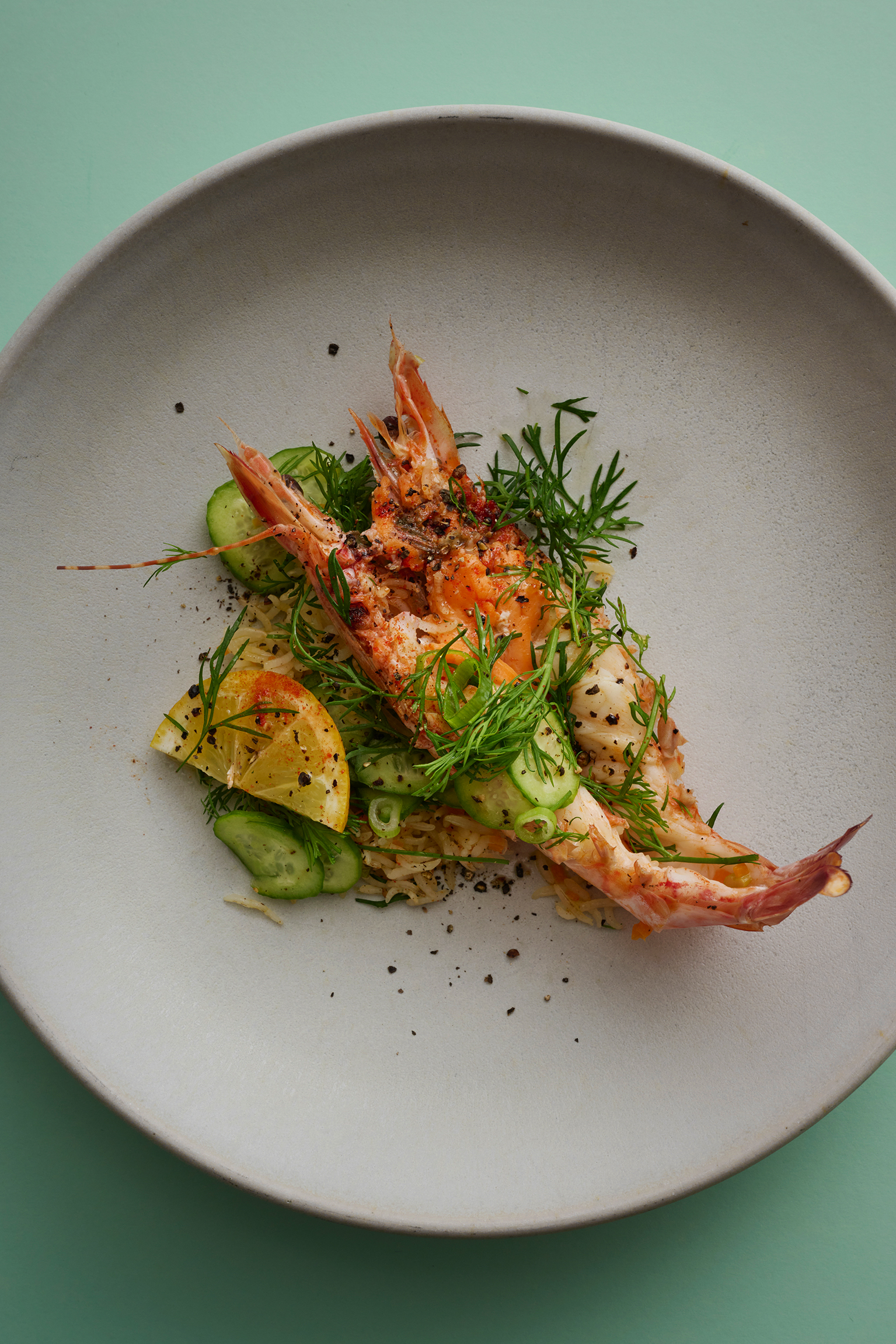 Two cooked prawns served with rice and garnished on a white plate.
