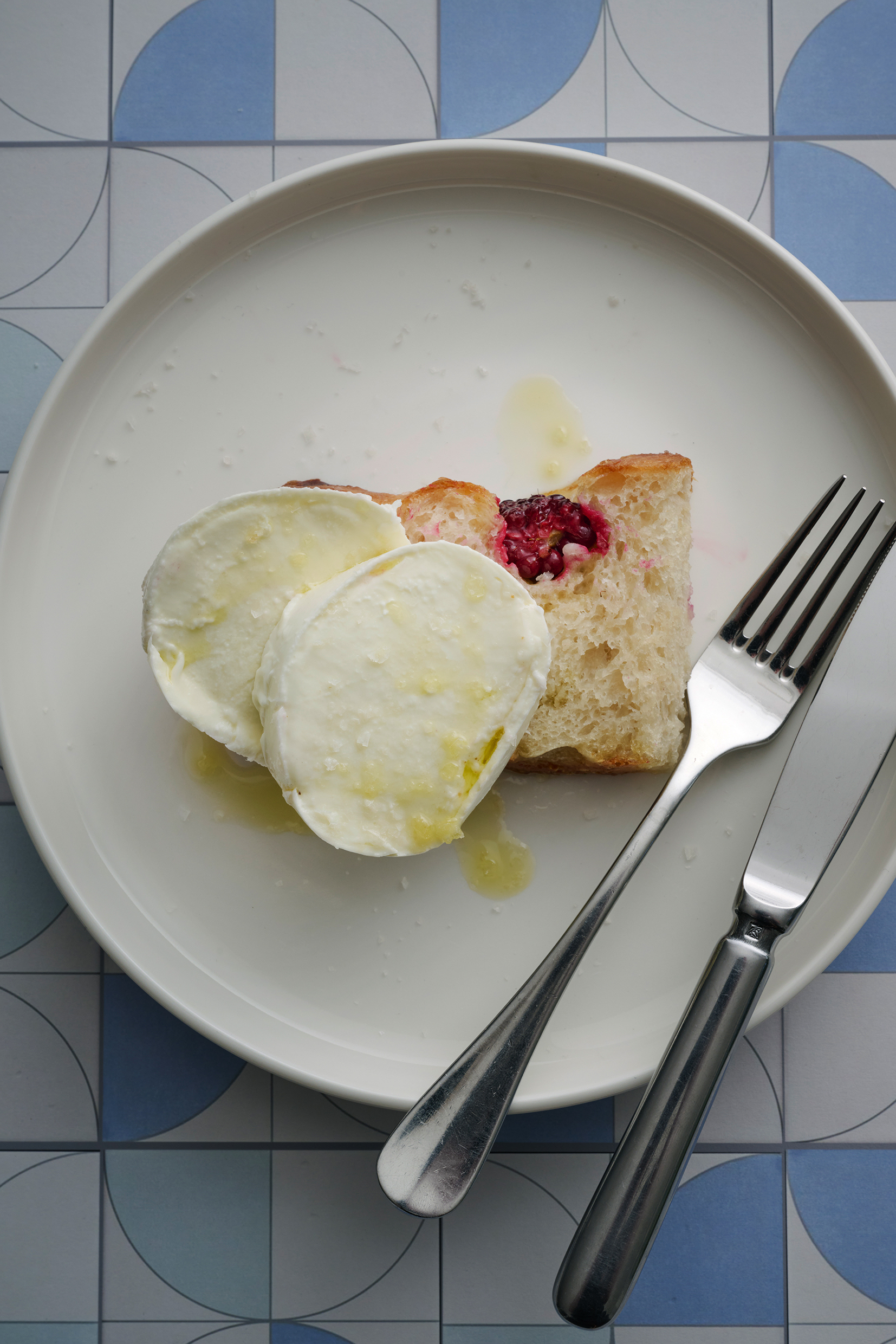 Sliced focaccia with buffalo mozzarella. Served on a white plate with a knife and fork.
