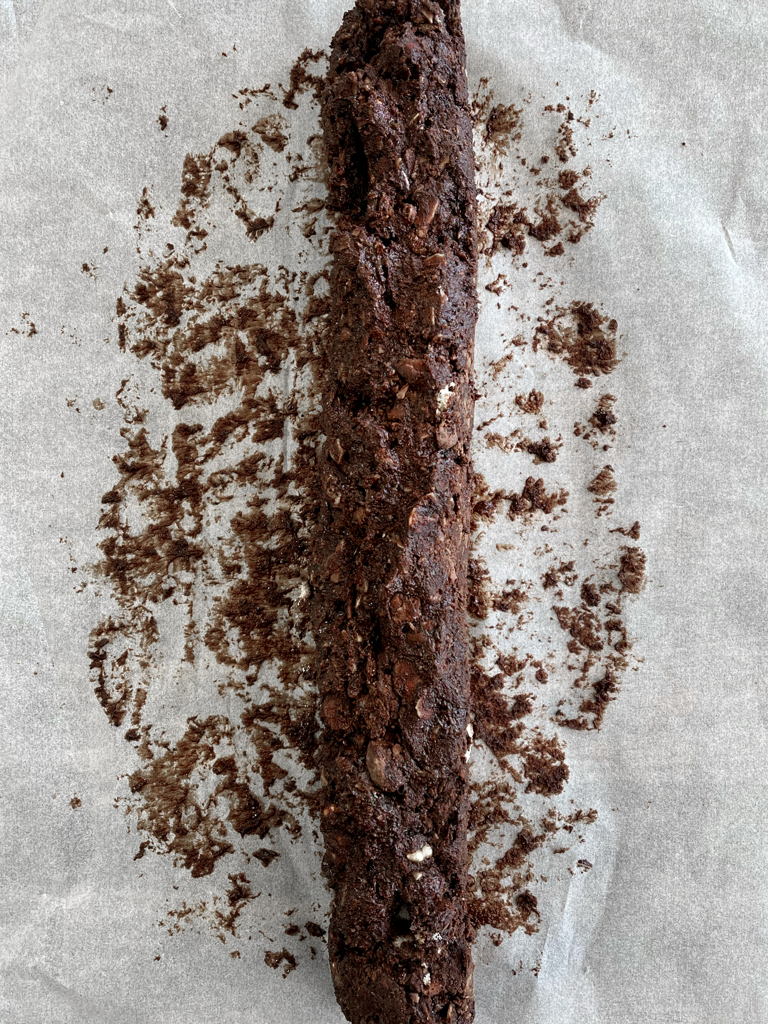 A brown log of nuts and chocolate rolled up on a sheet of baking paper