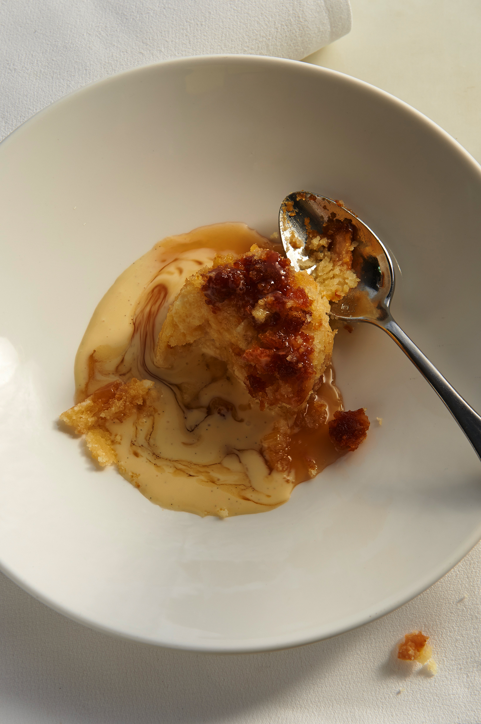 Ginger pudding with custard served in a white bowl and with a silver spoon.