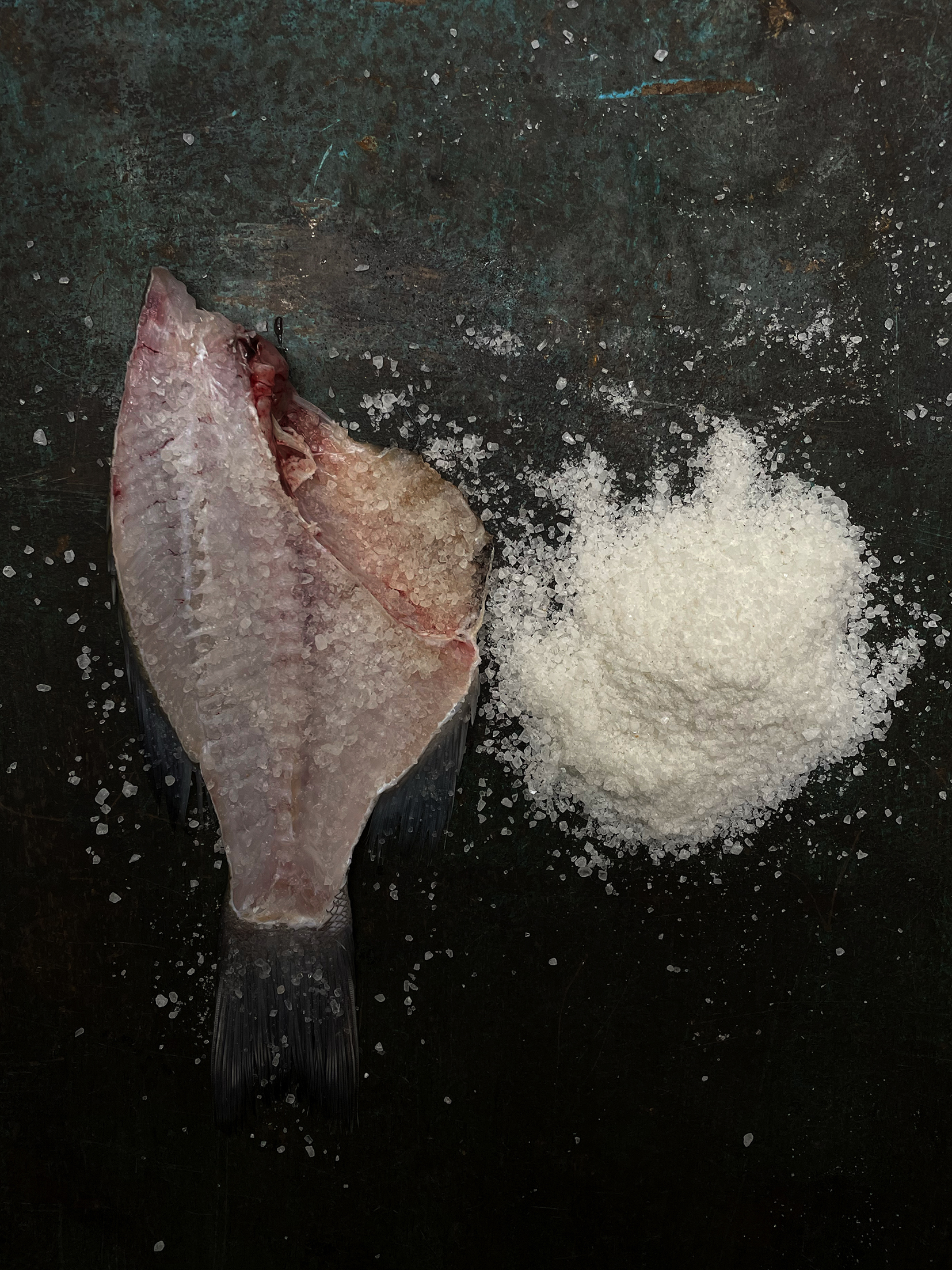 Raw fillet of fish laid out on a black table and beside a small pile of salt