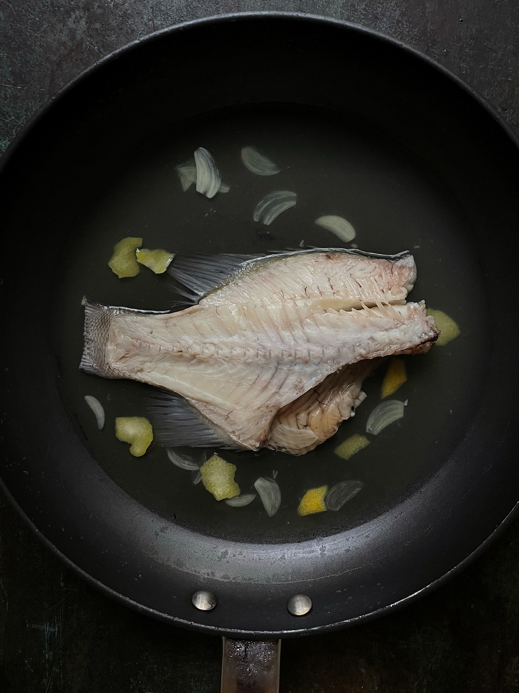 Fillet of fish in a black saucepan with slices of onion scattered around it