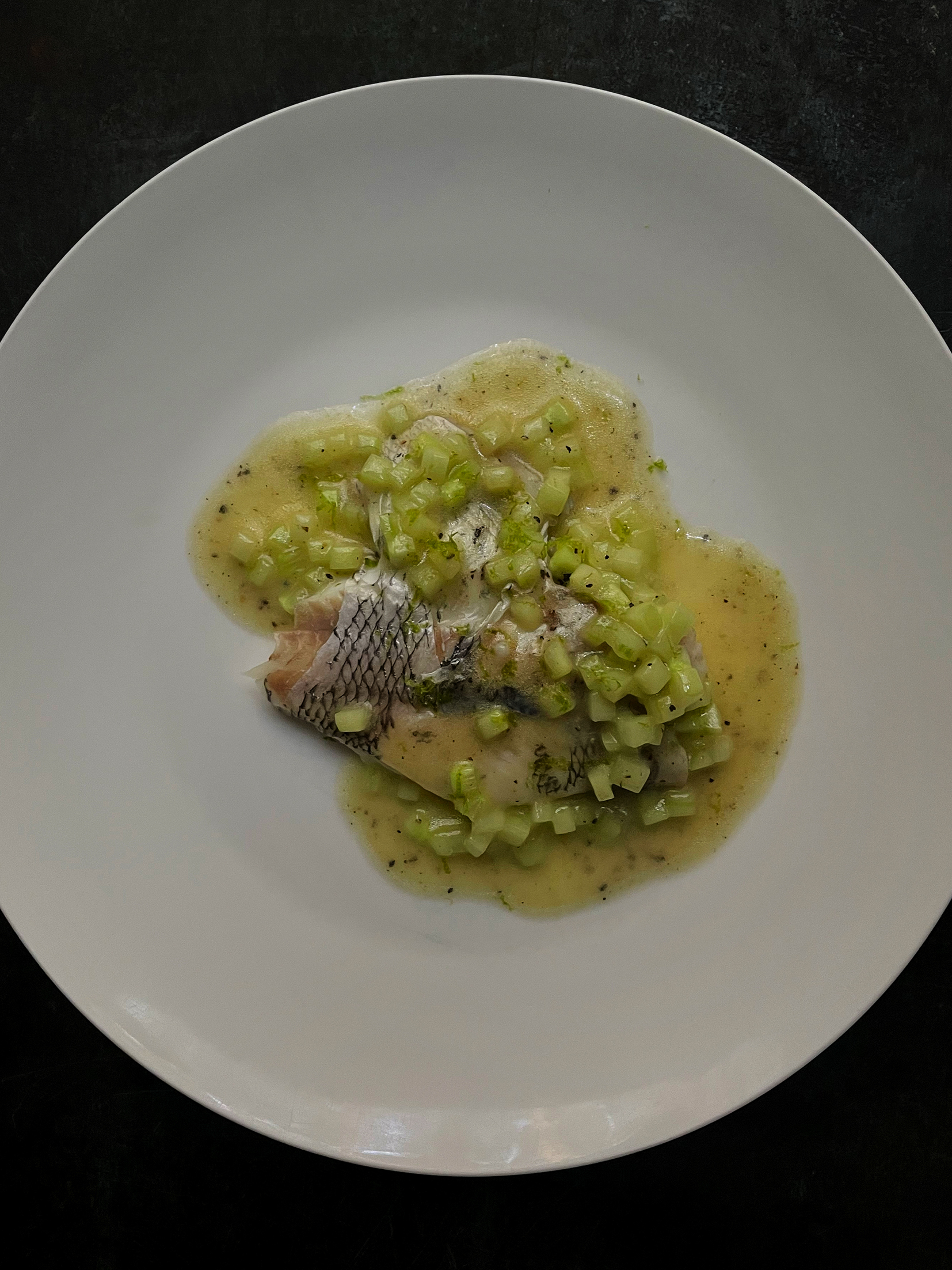 Fillet of fish on a white plate, dressed in diced cucumber and a yellow sauce.