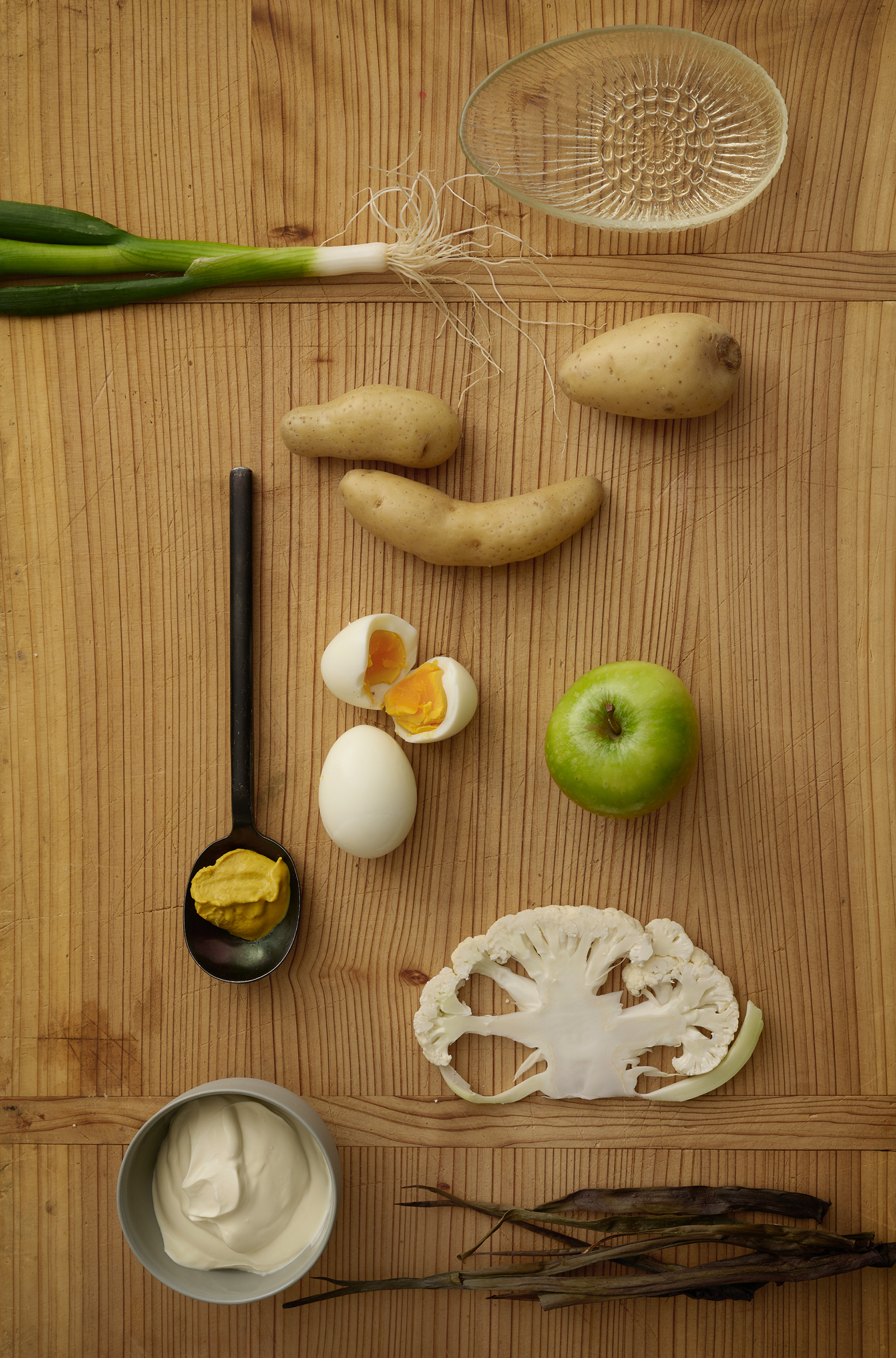 Potatoes, cooked eggs, an apple and cauliflower on a bench 