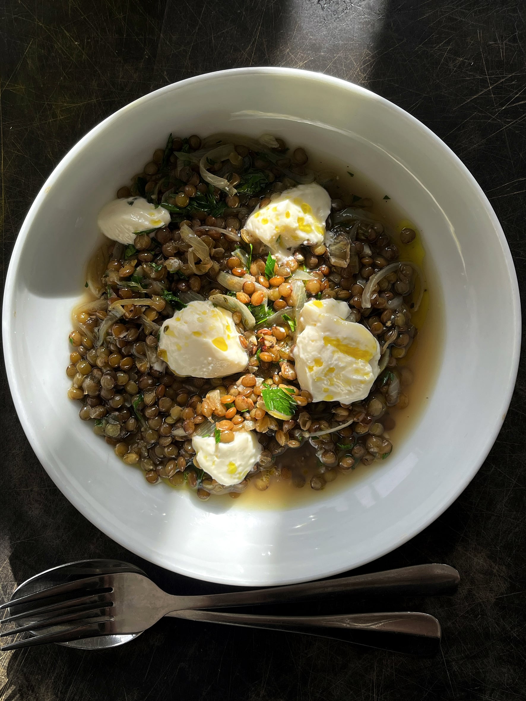 Braised lentils sit in a white bowl with caramelised brown onions and spoonfuls of curd to finish.