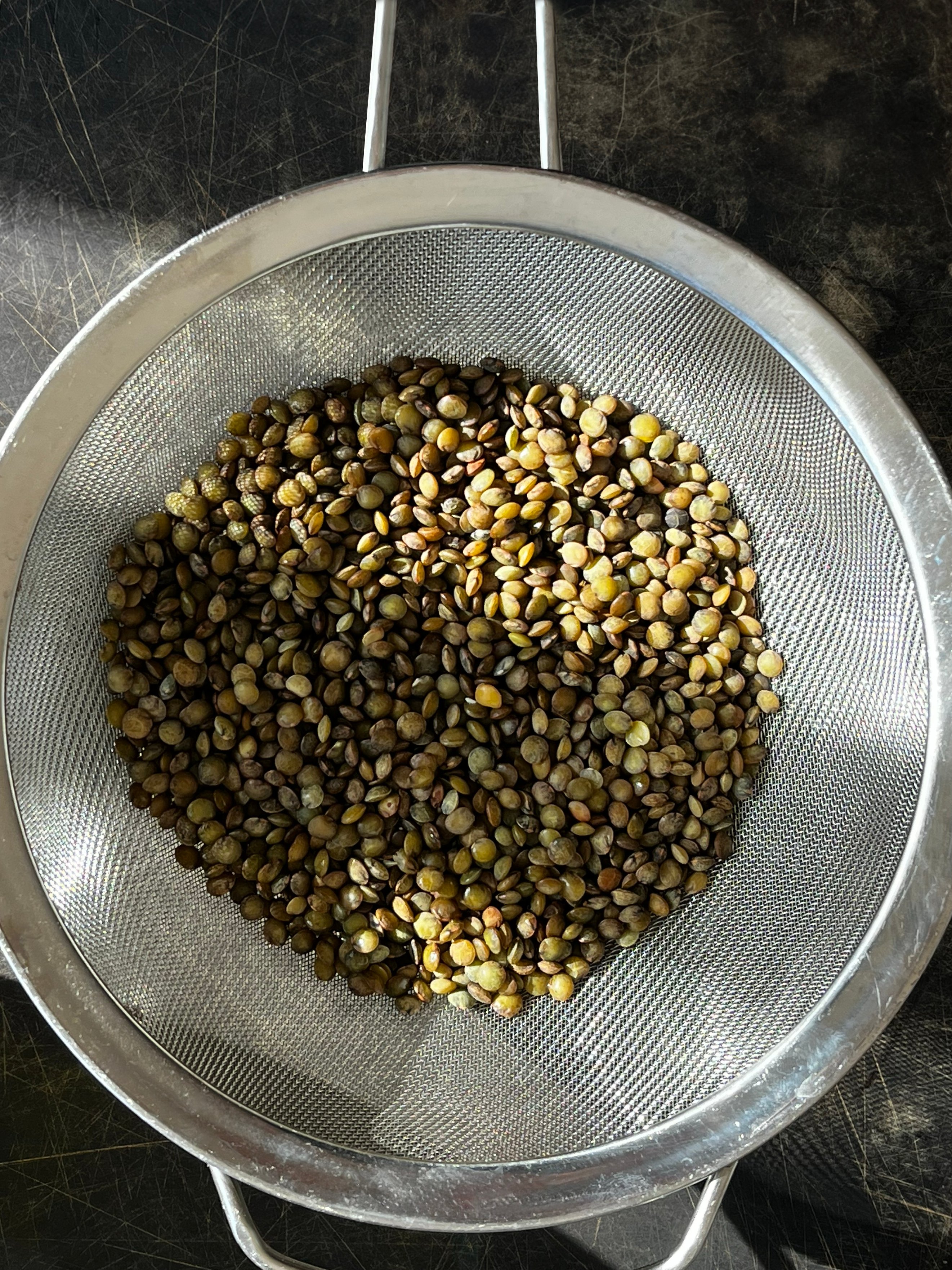 Brown and green lentils sit in a sieve. 