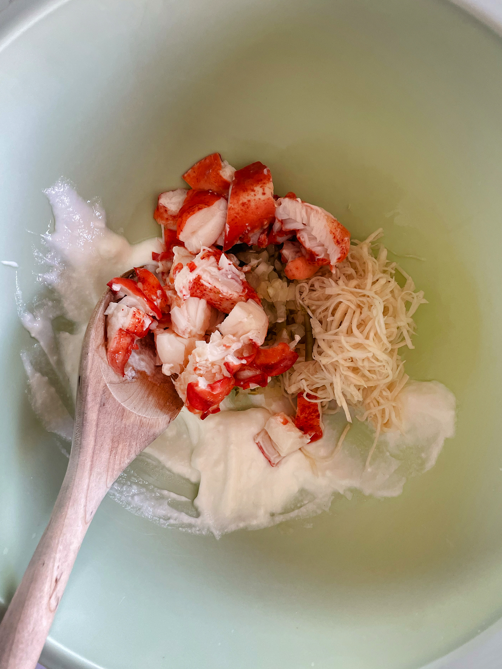 Shredded lobster and mayonnaise in a a mixing bowl with a wooden spoon.