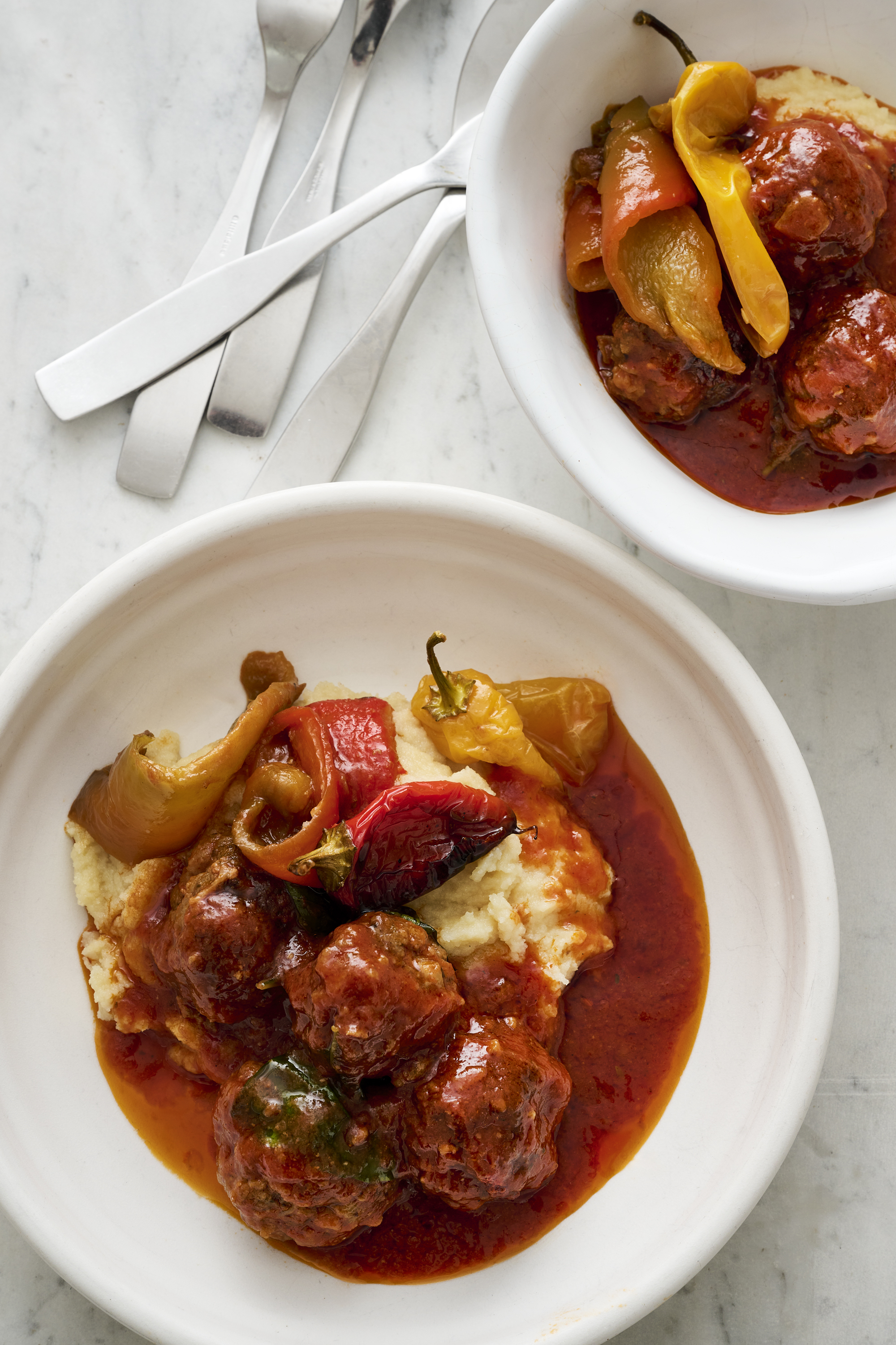Two bowls of meatballs in sauce sit on a bench top. 