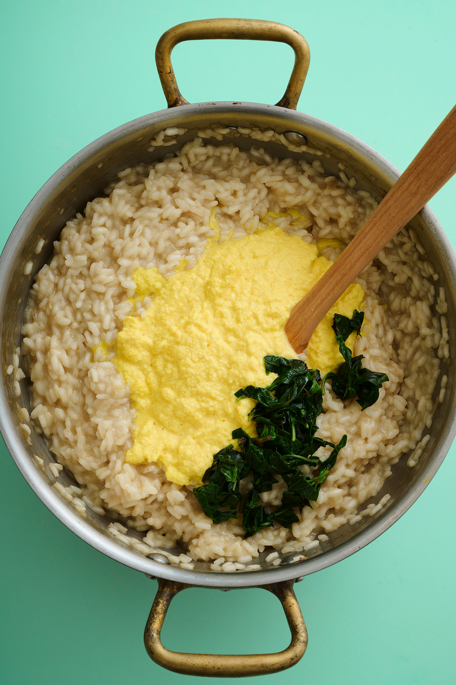 Rice, cheese and basil in a cooking pot with a wooden spoon.